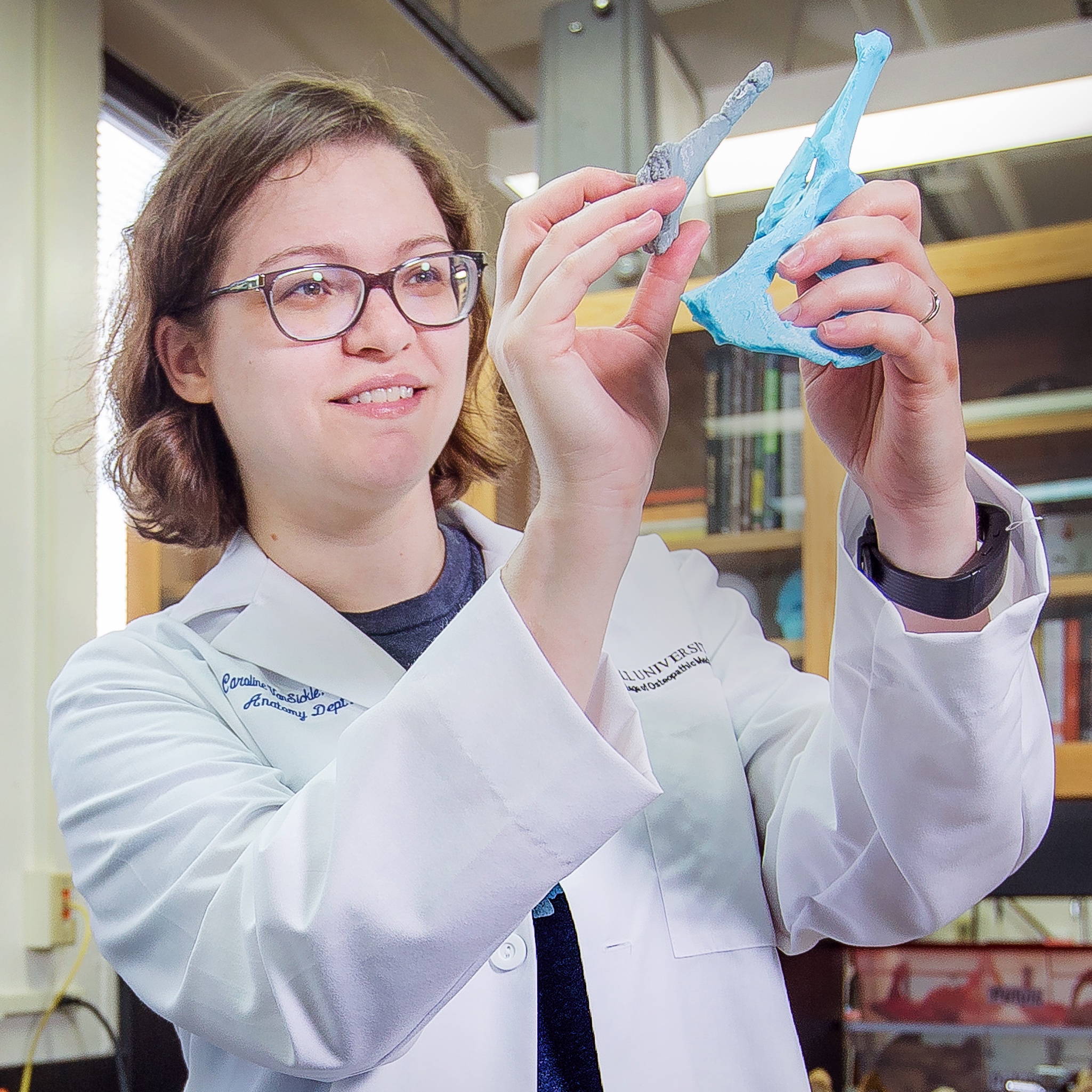 Woman in a white lab coat comparing two 3D-printed models of hominin pelvis fragments